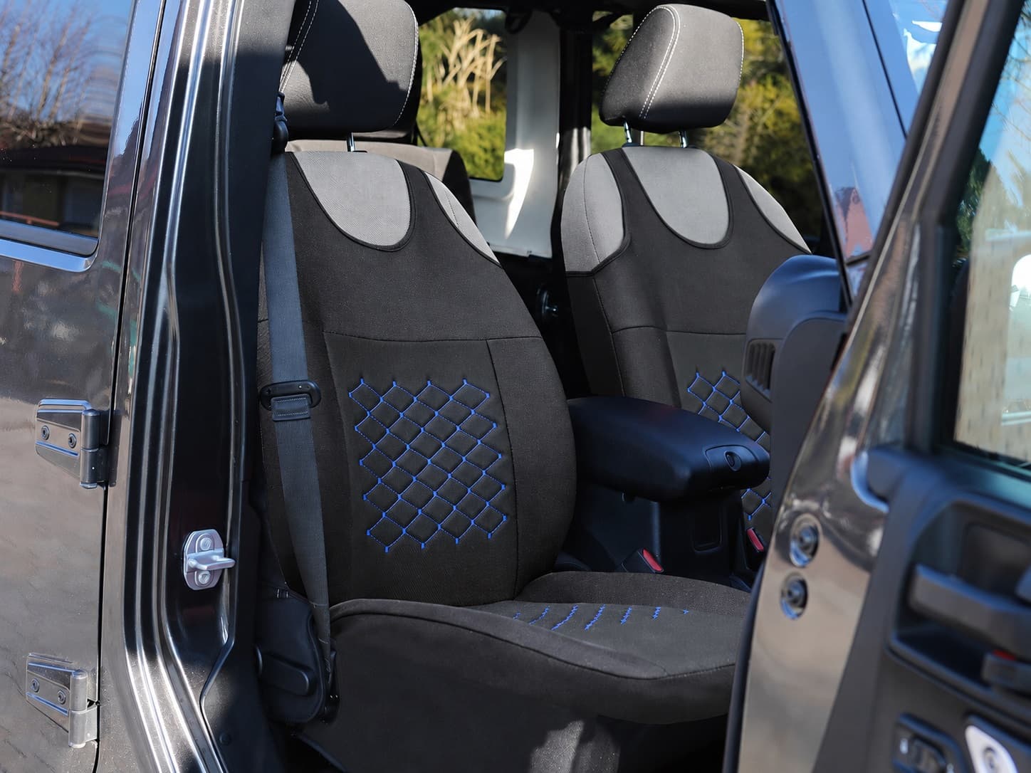 Housses de siège auto type T-shirt Motive noires avec surpiqûres bleues installées sur les sièges avant d’une voiture